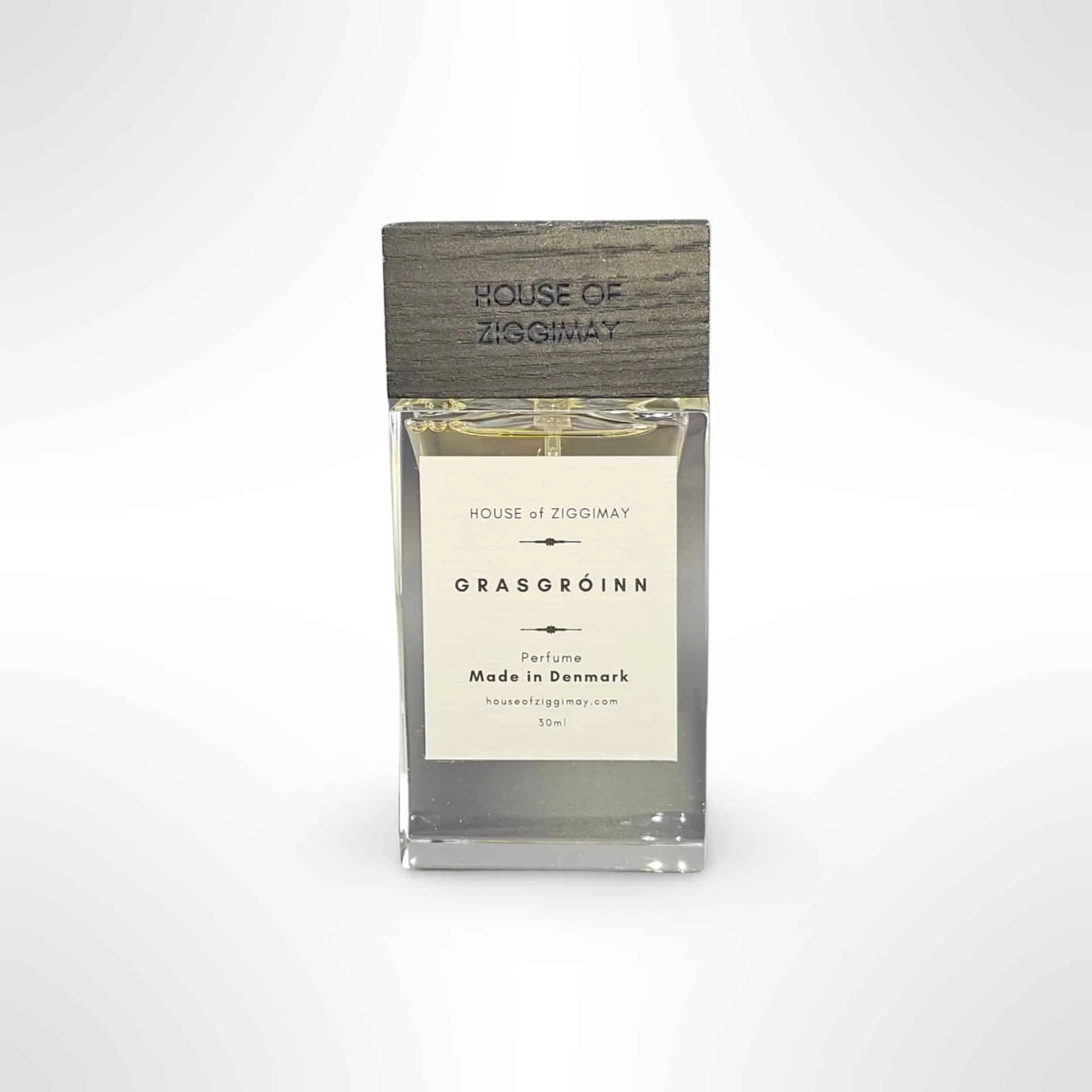 A rectangular glass bottle containing the Grasgróinn fragrance by House of Zigmig, adorned with a wooden cap featuring the brand's logo. The label highlights its Danish origin and states that it holds 30 ml of this exquisite perfume. A soft gradient background emphasizes the perfume's elegance.