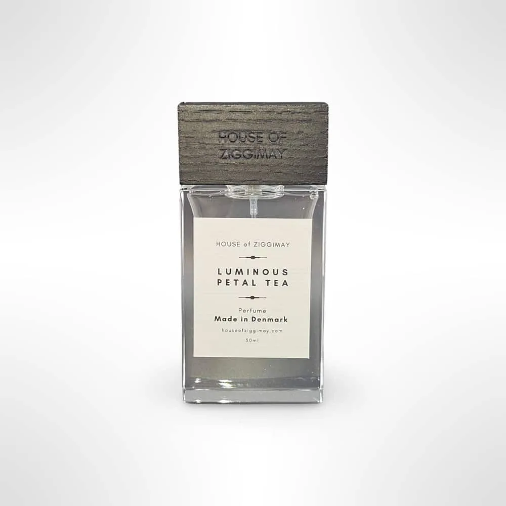 A rectangular glass bottle of niche perfume with a metallic cap, labeled HOUSE OF ZIGGIMAY and Luminous Petal Tea- Perfume - Made in Denmark. The 30ml bottle features a minimalist design with a light background.