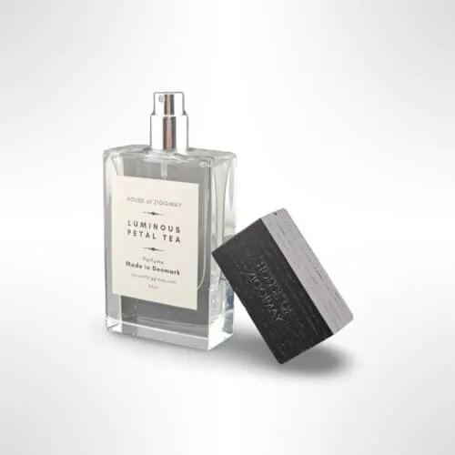 Homepage A variety of elegant perfume bottles in different shapes, sizes, and shades of pink, gold, and clear glass are arranged on tiered white shelves, reflected on a glossy surface perfect for exploring perfume layering or discovering your signature scent.