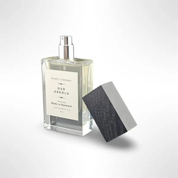 The image shows a bottle of House of Zigbimay Oud Absolu perfume with a sleek, minimalist design. The bottle is made in Denmark and features a wood-textured black cap. It is set against a white background.