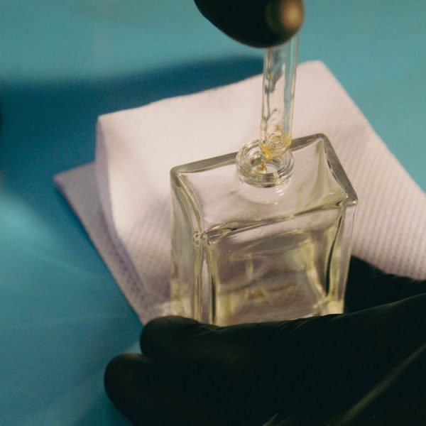 a person in black gloves is putting something in a square glass bottle