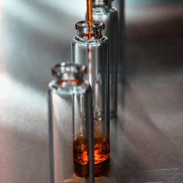 A variety of elegant perfume bottles in different shapes, sizes, and shades of pink, gold, and clear glass are arranged on tiered white shelves, reflected on a glossy surface perfect for exploring perfume layering or discovering your signature scent.