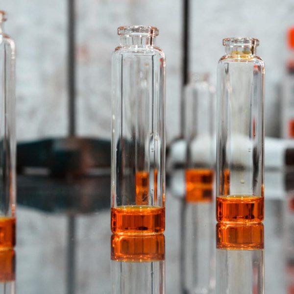 A variety of elegant perfume bottles in different shapes, sizes, and shades of pink, gold, and clear glass are arranged on tiered white shelves, reflected on a glossy surface perfect for exploring perfume layering or discovering your signature scent.